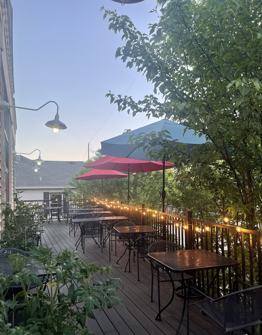 The Schnitz rooftop deck at golden hour — red and navy umbrellas, string lights and a view over Ada Village